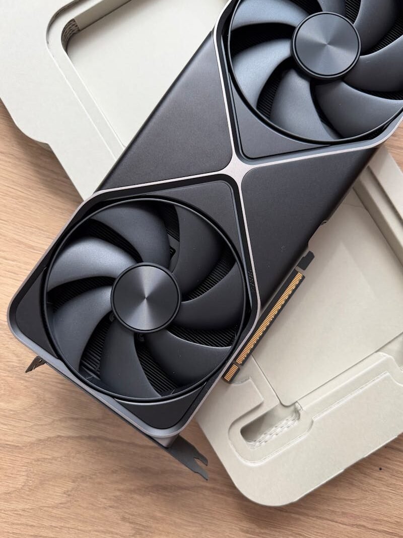 Close-up of a black graphics card with dual fans on wooden desk in minimalist packaging.